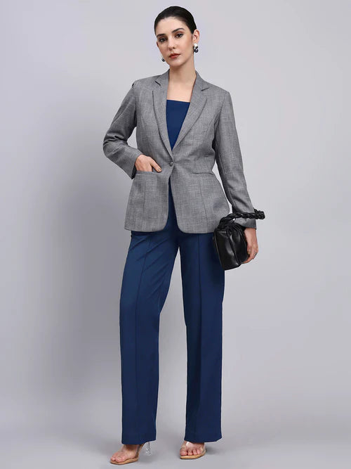 Woman wearing a gray blazer and blue pants with a black handbag on a light gray background