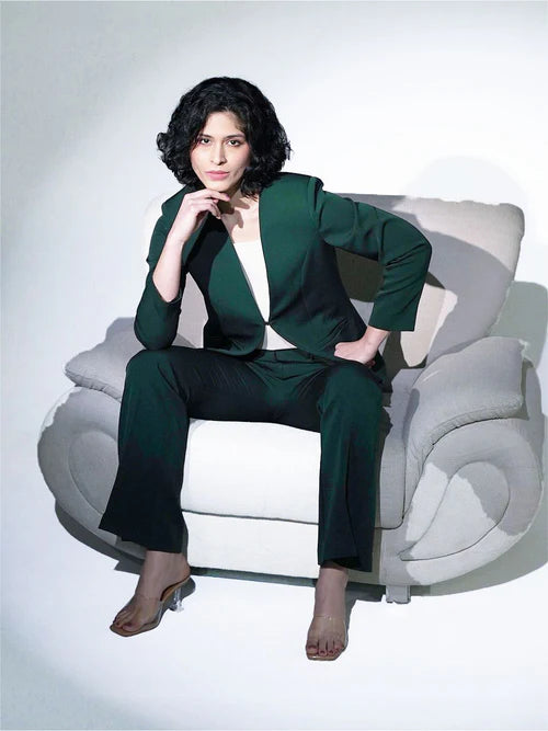 Woman in a green suit sitting on a white chair against a white background