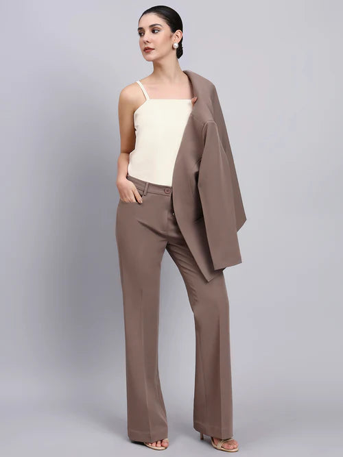 Woman wearing a beige top and brown pants with a matching blazer on a gray background
